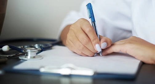 Médecin écrivant des notes dans un dossier patient en consultation